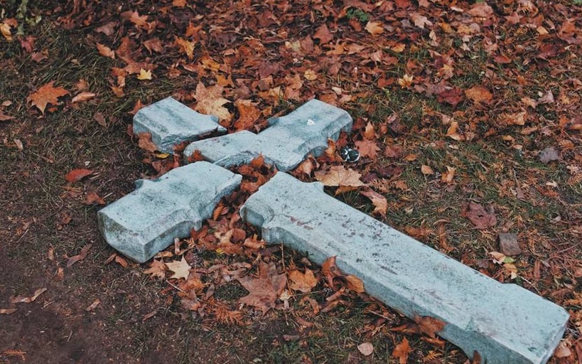 Gebroken kruis liggend op de grond in herfstblaadjes